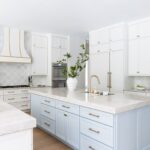 white kitchen with white and light blue shaker cabinets featuring a white Hoodsly wooden range hood with brass strapping