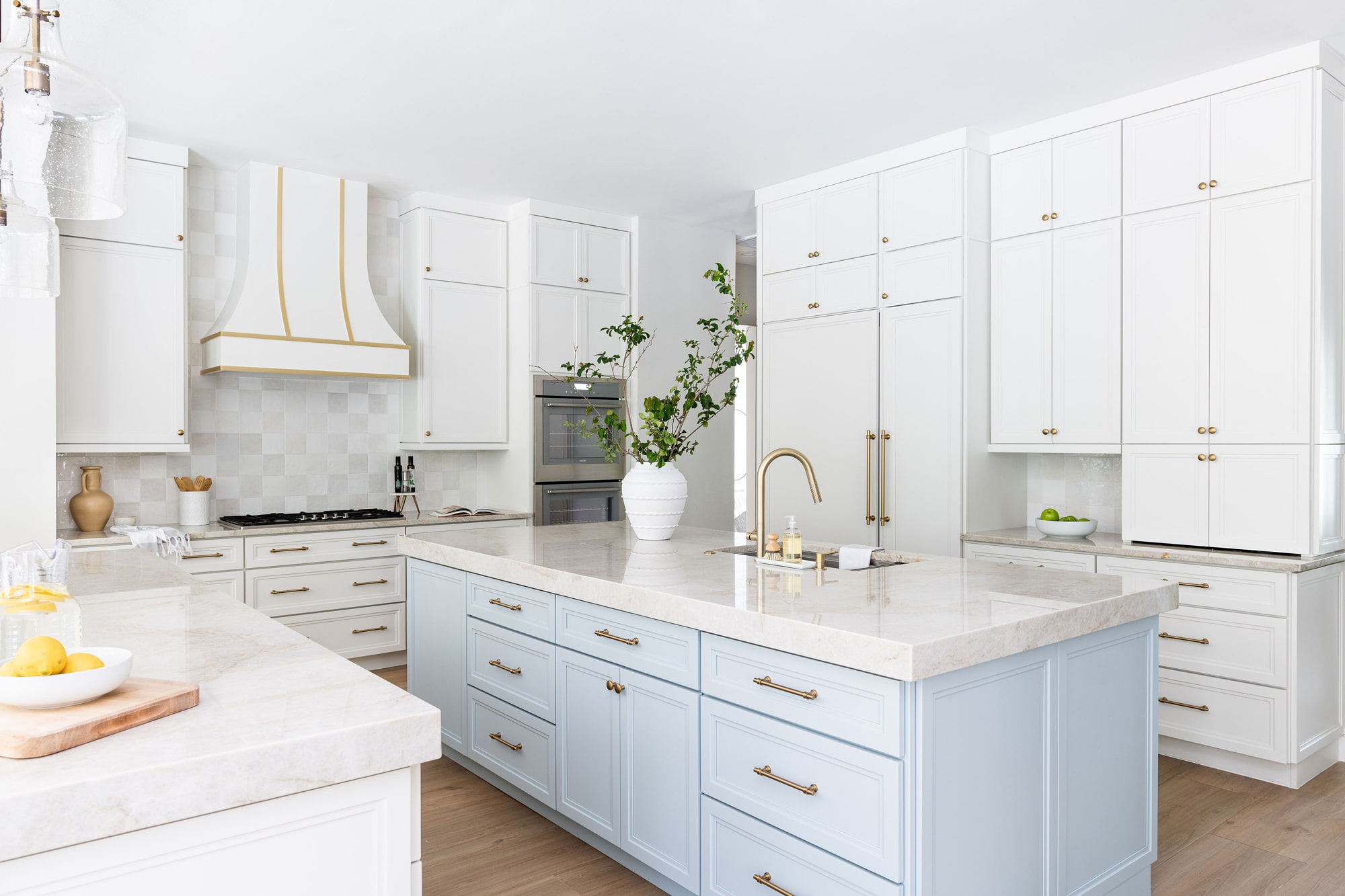 white kitchen with white and light blue shaker cabinets featuring a white Hoodsly wooden range hood with brass strapping