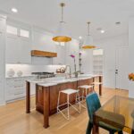 white kitchen with white shaker cabinets and gold accents featuring a white Hoodsly angled range hood with walnut band